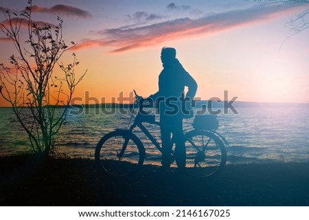 Silhouette of a female cyclist and a bicycle against the backdrop of a sunset over a lake. Sports action.