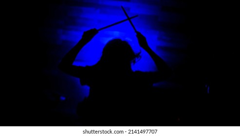 Silhouette of female drummer holding drum sticks up in the air during a show. Professional drummer plays drums perfectly on stage during a show. Girl drummer concert concept.