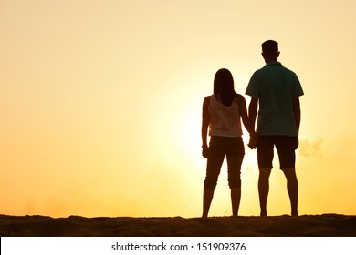 Silhouette of a female and male holding hands at sunset