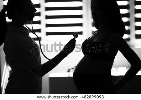 Silhouette female medicine doctor holding stethoscope to pregnant woman standing for encouragement, empathy, cheering,support, medical examination. New life of abortion concept. B/W style