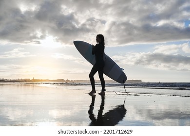 Silhouette Female Surfer Standing With Her Surf Board In Front Of The Ocean During The Sunset