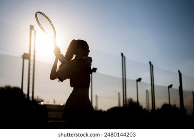 silhouette of a female tennis player executing a backhand swing during a sunset match on an outdoor court - Powered by Shutterstock