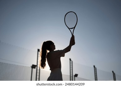 silhouette of a female tennis player executing a backhand swing during a sunset match on an outdoor court - Powered by Shutterstock