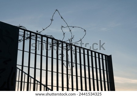 silhouette of a fence with barbed wire against the light, symbol of borders, closures, imprisonments, imprisonments, and dramatic moments in the history of humanity