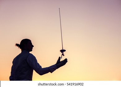 Silhouette of fencer man throwing up his fencing sword on a sunset background