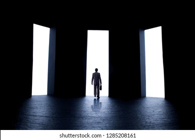 Silhouette Figure Of A Young Man In A Business Suit With A Briefcase In Front Of Three Open Doors With Light, Person Decides What Path To Choose, The Concept Of Life Choices And Business