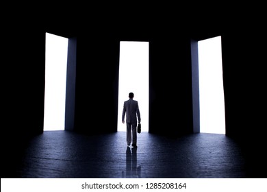 Silhouette Figure Of A Young Man In A Business Suit With A Briefcase In Front Of Three Open Doors With Light, Person Decides What Path To Choose, The Concept Of Life Choices And Business