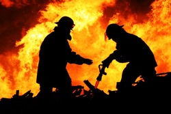Silhouette Of Firemen Fighting A Raging Fire With Huge Flames Of Burning Timber
