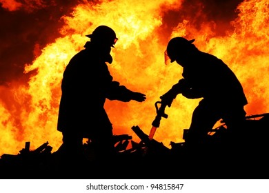 Silhouette Of Firemen Fighting A Raging Fire With Huge Flames Of Burning Timber