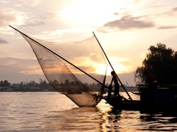 Silhouette Of A Fisherman Fishing On A Boat With Fishnet At Sunset On The Mekong River. Mekong Delta, Can Tho, Vietnam
