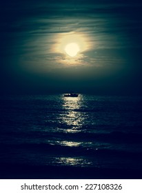 Silhouette of the fisherman or leisure boat sailing toward the moon. Dark sky and clouds. Moonwalk. Reflection in water. Beautiful seascape in the night. Harmony with nature idea. Mystery background.