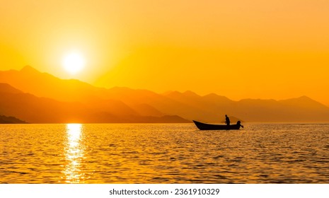 Silhouette of a fishing boat with a fisherman fishing in the orange sunset of Shkoder lake in Shiroka and mountains. Albania - Powered by Shutterstock