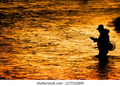 Silhouette of Fishing Flyfishing rod reel in river with golden sunlight - Powered by Shutterstock