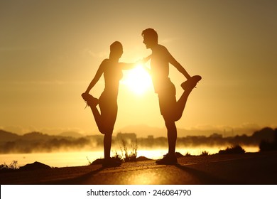 Silhouette of a fitness couple profile stretching at sunset with the sun in the background - Powered by Shutterstock