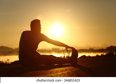 Silhouette Of A Fitness Runner Man Stretching At Sunset With The Sun In The Background