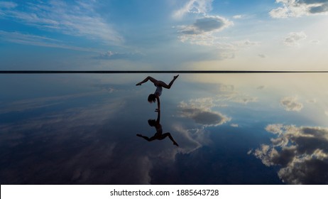 Silhouette of a flexible graceful girl in the mirror reflection of the sky and sea, handstand in harmony with nature