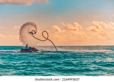 Silhouette of a fly board rider at sea. Professional rider do tricks in the blue lagoon. Tropical watersport equipment. Sunset sea view, summer outdoor sport, recreational activity, amazing splash