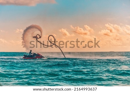 Silhouette of a fly board rider at sea. Professional rider do tricks in the blue lagoon. Tropical watersport equipment. Sunset sea view, summer outdoor sport, recreational activity, amazing splash
