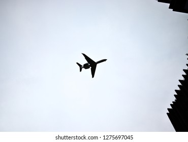 Silhouette Of Flying Gulfstream V Twin Engine Business Jet From Below Framed By Buildings