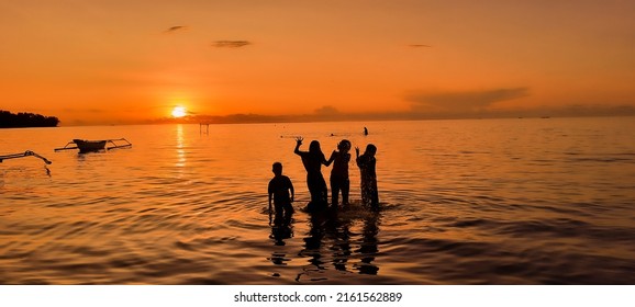 Silhouette of four children playing on the beach with sunset background and boats. Sunset on the beach. Silhouette of childrens. Sunset Beach Vacation Outdoor Summer holiday Background. - Powered by Shutterstock