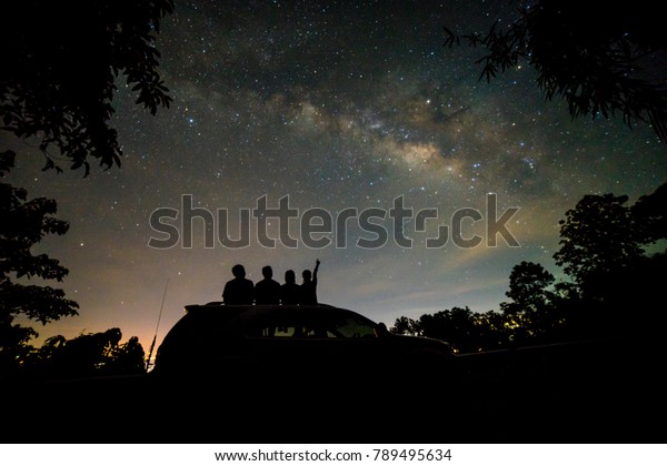 Silhouette of four friends watching milky\
way and pointing to the star on roof top of SUV\
car