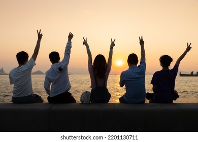 Silhouette Of Four Youngsters Students Boy And Girl Chat And Have Fun And Take Photos During Sunset In West Kowloon Waterfront Promenade, Hong Kong In Evening. Back Light Shot