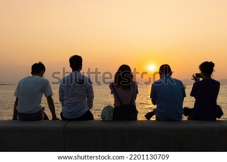 silhouette of four youngsters students boy and girl chat and have fun and take photos during sunset in West Kowloon Waterfront Promenade, Hong Kong in evening. back light shot
