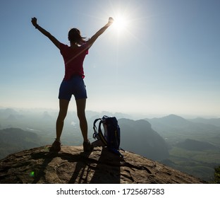 Silhouette of free cheering woman hiker open arms at mountain  top cliff edge