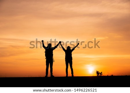 Silhouette of freedom backpacker,person back view standing with raised hand in successful job.Couple of love with sunset background in Thailand.Freedon,release and success concept.