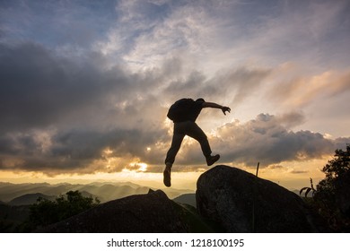 Silhouette Freedom-young man is jumping over precipice between two rocky mountains at sunset. - Shutterstock ID 1218100195