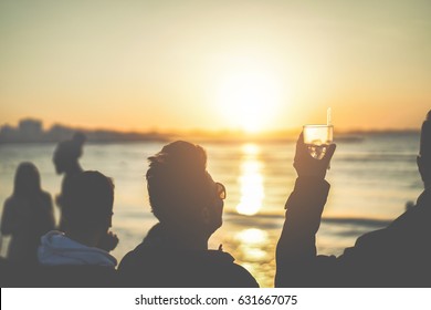 Silhouette of friends drinking cocktail on beach sunset party - Young people having fun together outdoor - Youth concept - Focus on glass - Matte filter - Powered by Shutterstock