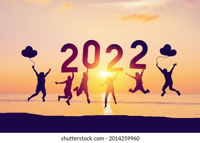 Silhouette friends jumping and holding number 2022 on sunset sky abstract background at tropical beach. Happy new year and holiday celebration concept. Vintage tone color style.
