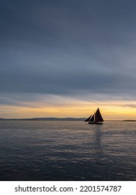 Silhouette of Galway hooker type wooden boat sailing from harbor at stunning sunset time. Hobby and water sport. Dark and moody sky and dark water of Galway bay, Ireland.