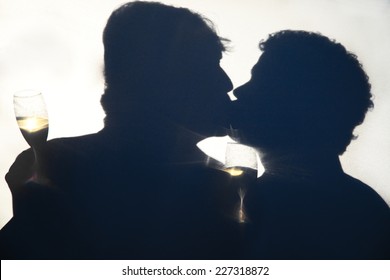 Silhouette Of Gay Men Kissing On Their Wedding Day, Holding Champagne Glasses Behind An Opaque Screen.  