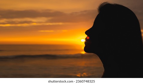 Silhouette of a girl backlit, kissing the sun in front of the se