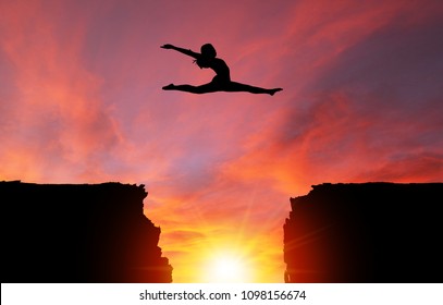 Silhouette of girl dancer in a split leap over dangerous cliffs with sunset or sunrise background and copy space. Concept of faith, conquering adversity, taking risk; challenge, courage, determination
