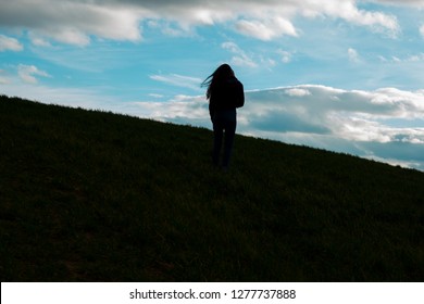 silhouette of a girl with long hair in the wind on a hill with the background of a blue sky