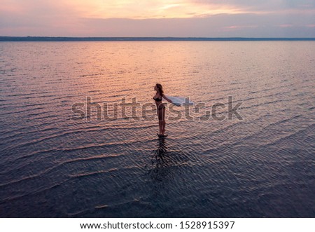 Silhouette of a girl in the middle of lake at sunset. Beautiful girl posing alone in shallow water with light ripples
