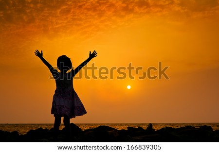 Silhouette of a girl on a beach with arms rised up during the sunset.