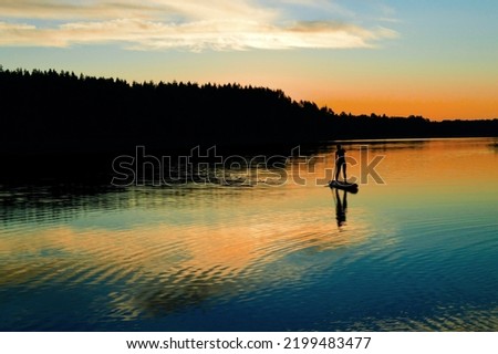 Silhouette of a girl on a SUP board on the river. Evening, beautiful sunset of pink, yellow and blue hues, twilight, picturesque landscape. Postcard, wallpaper, background. Summer, water sports