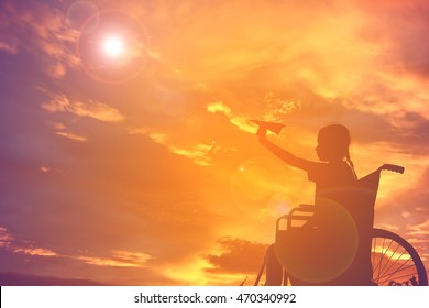 Silhouette a girl on wheelchair with rocket paper in the sunset