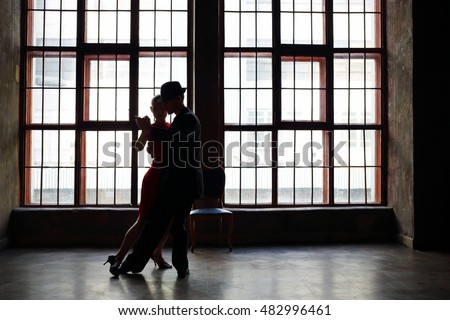 Silhouette of girl in red dress and man in black suit dancing tango
