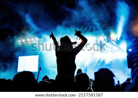 Silhouette of girl at rock concert crowd in front of bright stage lights. Pleasure at summer music fest