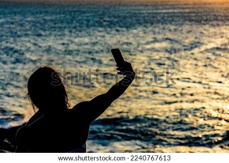 Silhouette of girl with smartphone taking selfie in the summer during the sunset in Salvador city, Bahia