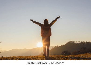 Silhouette of girl spreading arms standing on a mountain and looks at the sunset - Powered by Shutterstock