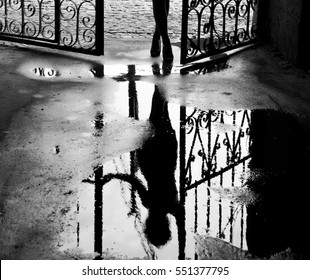 Silhouette of a girl standing in the street. Creative photo of rain mood. Woman's reflection on a wet pavement after the rain. The legs of a woman, black and white background.