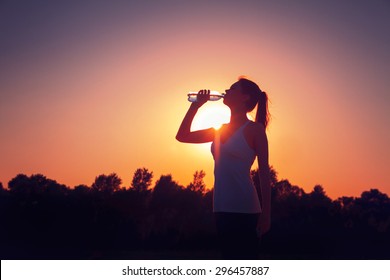 Silhouette of a girl at sunset with a bottle of water