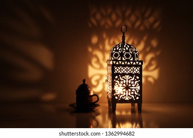 Silhouette of glowing Moroccan ornamental lantern with bronze tea cup. Decorative golden shadows. Greeting card, invitation for Muslim holy month Ramadan Kareem. Festive night  background.