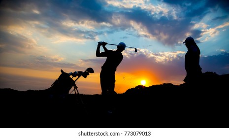 Silhouette of a golf couple playing golf at sunset