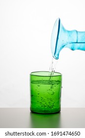 Silhouette Of A Green Glass, Water Is Poured From A Blue Turquoise Bottle, Against A White Background With Reflection In Zurich, Europe, Switzerland.